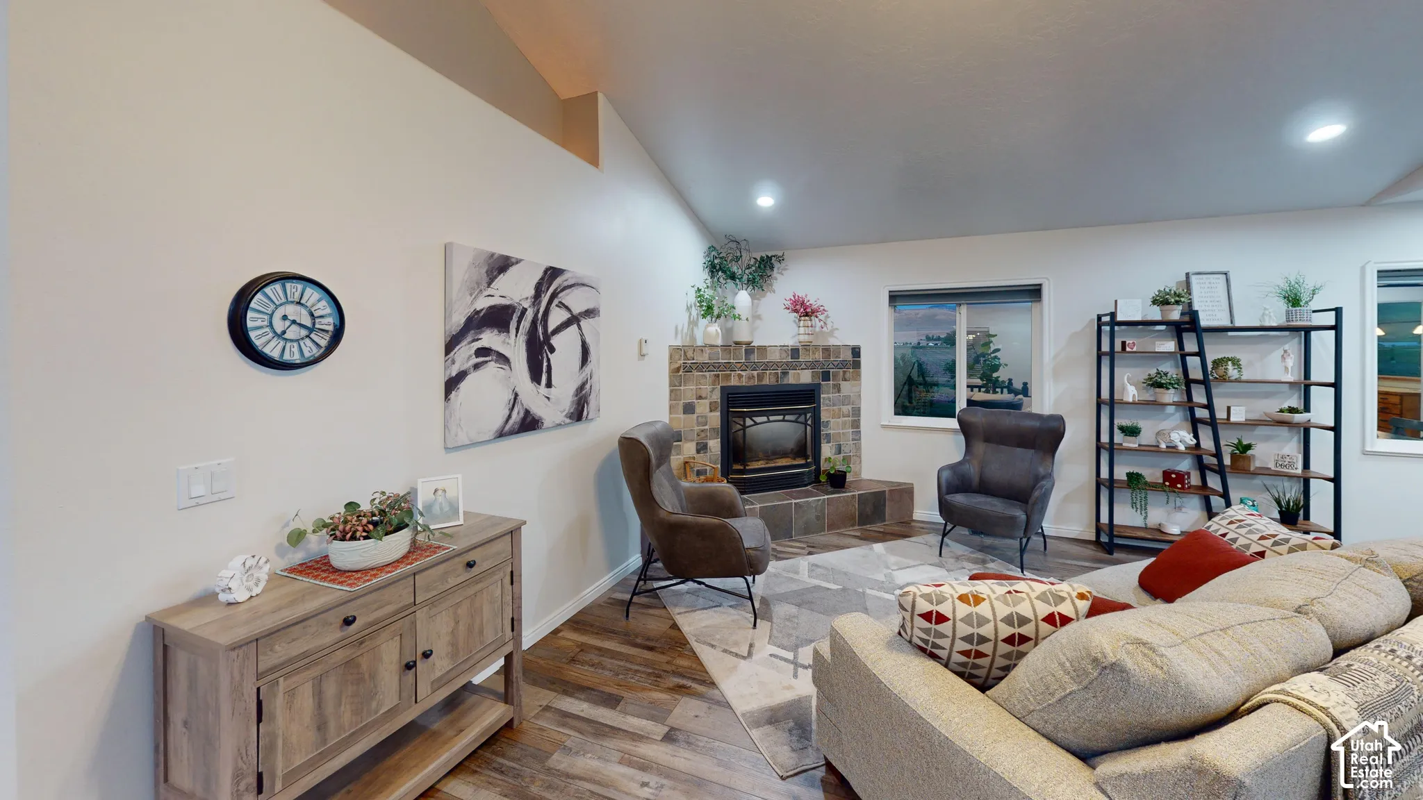 Vaulted ceiling, stone-clad fireplace with hearth, recessed lighting, wood-finish flooring, and white walls
