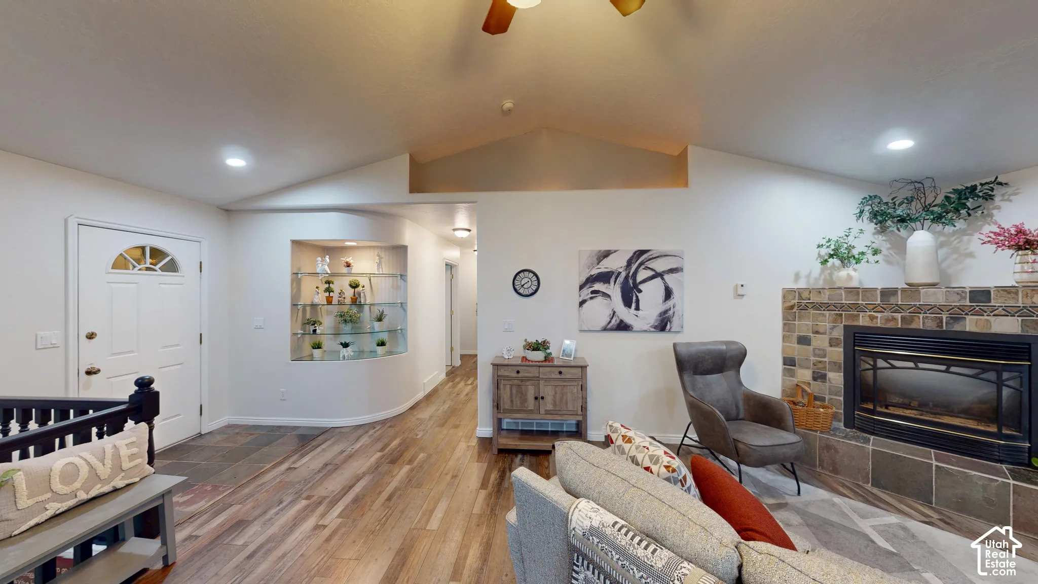 Vaulted ceiling with recessed lighting, wood-finish flooring, tiled fireplace with hearth, built-in display shelving, and an entry door with an arched window