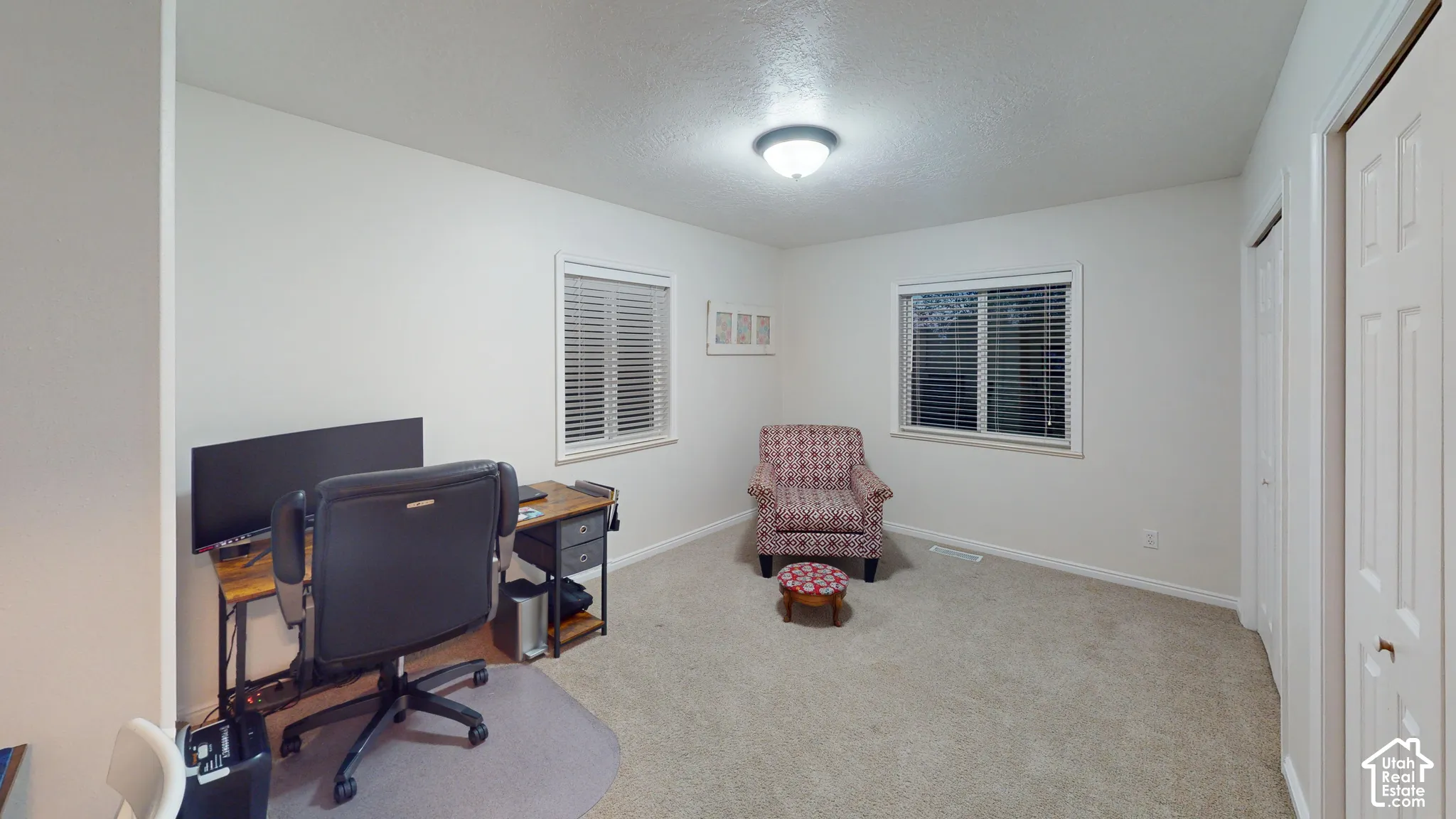 Light-colored carpeting, two windows with blinds, flush-mount ceiling light fixture, and white bi-fold closet doors