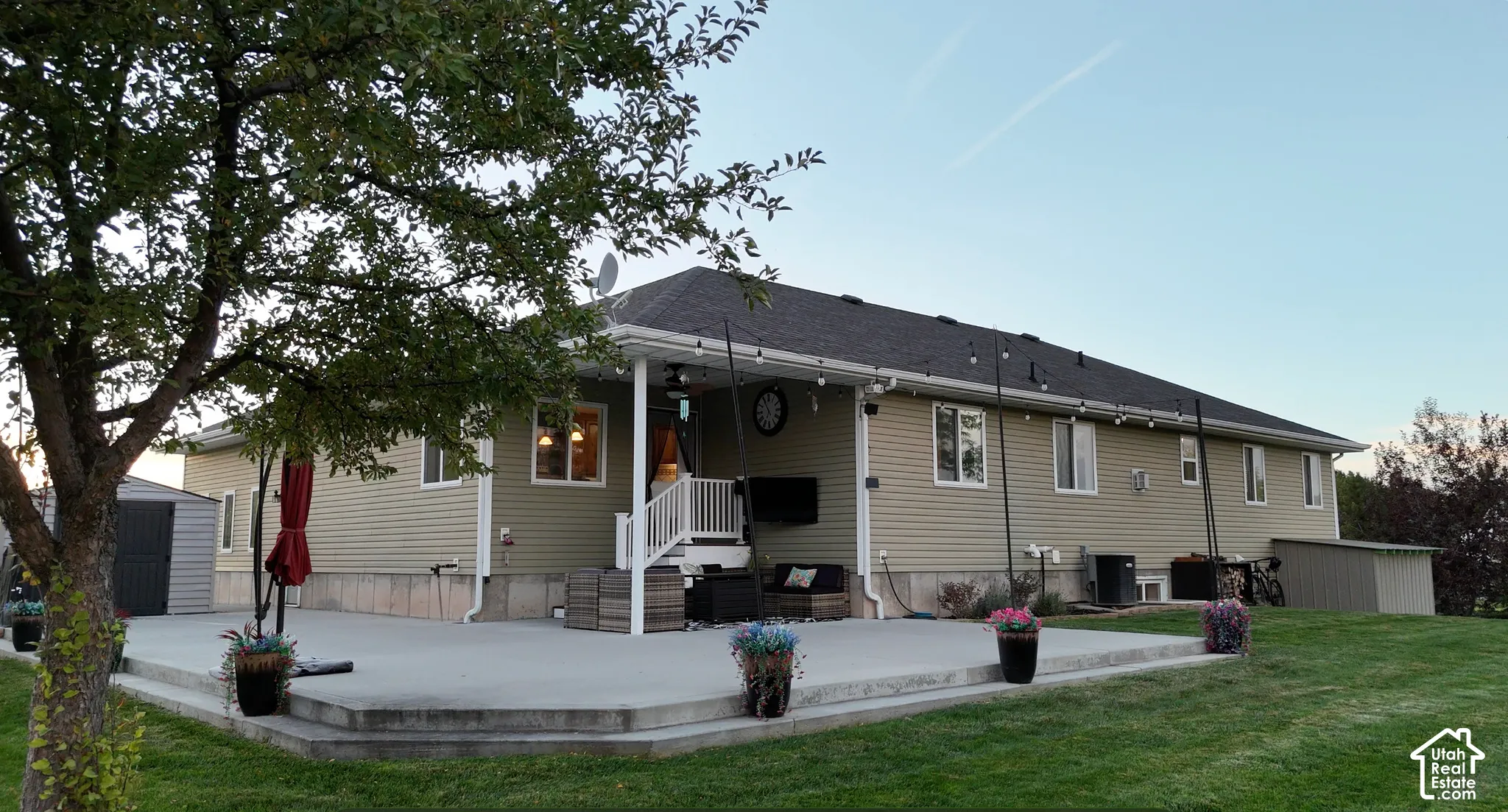 Expansive concrete patio with tiered steps, covered porch, multiple windows, and a manicured lawn