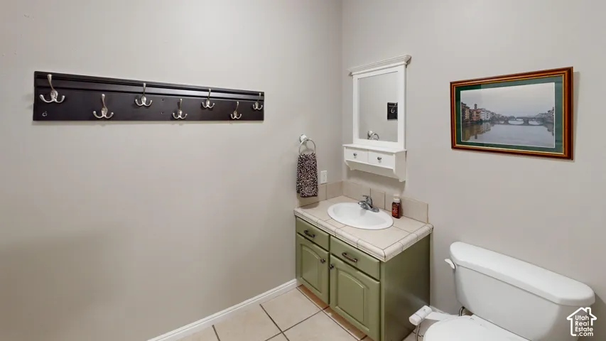 Tile flooring, single basin sink, white toilet, vanity with storage, wall-mounted mirror