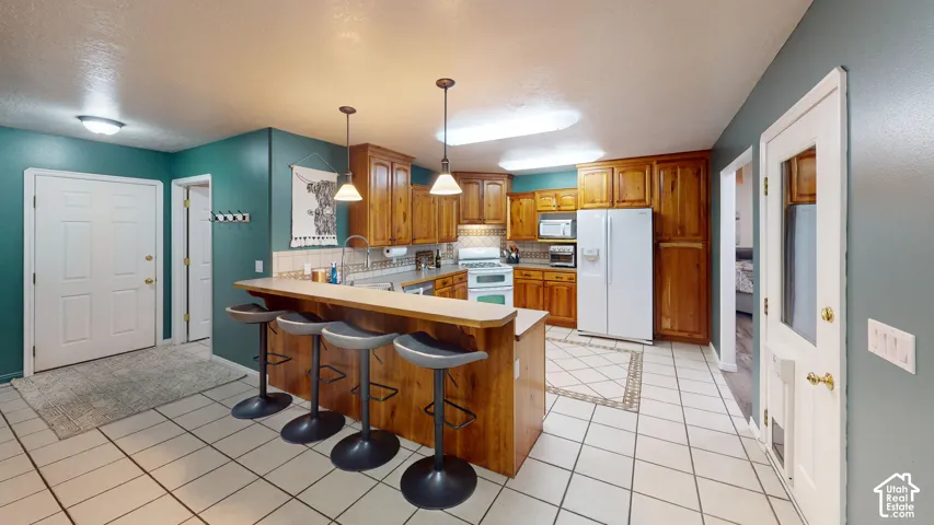 Kitchen featuring wood-finish cabinetry, white appliances, and a breakfast bar with pendant lighting