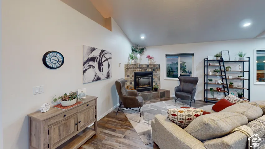 Vaulted ceiling, stone-clad fireplace with hearth, recessed lighting, wood-finish flooring, and white walls