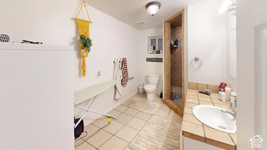 Tile flooring, vanity with integrated sink, tiled countertop, and a walk-in shower with tiled walls