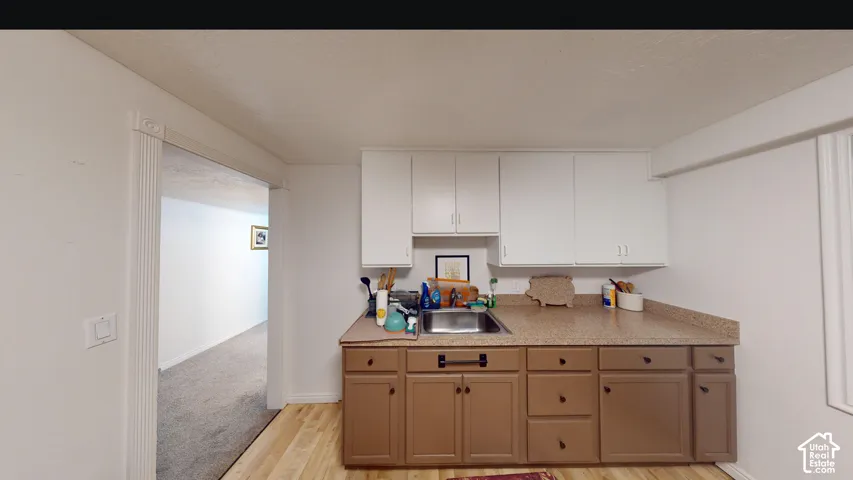Kitchenette featuring upper white cabinetry, lower wood-finish cabinetry, a stainless steel sink, and a speckled countertop