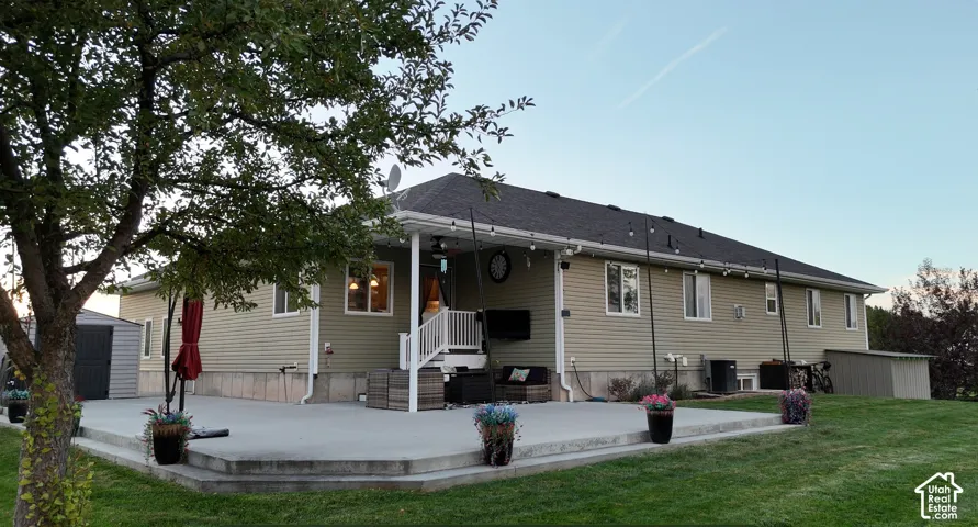 Expansive concrete patio with tiered steps, covered porch, multiple windows, and a manicured lawn