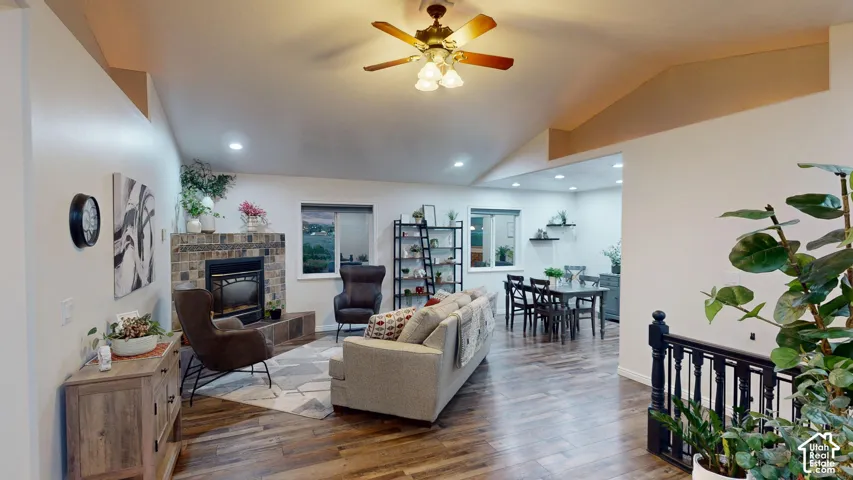 Vaulted ceiling with a ceiling fan, a fireplace with a stone surround, recessed lighting, and wood-finish flooring