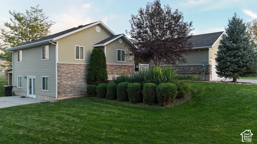 Exterior siding, stone-finish foundation, mature landscaping, paved patio, and attached garage
