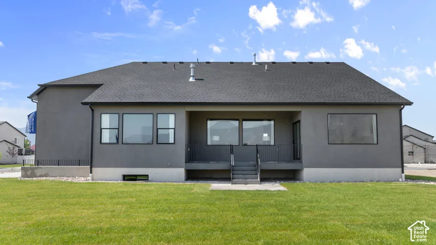 Expansive backyard featuring a manicured lawn, dark gray stucco exterior, dark gray shingle roof, large windows with black frames, and a covered patio with metal railings