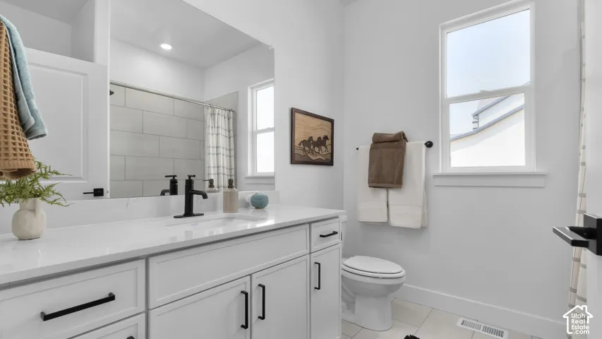 Bathroom featuring a white vanity with black hardware, a large mirror, a white toilet, and a window