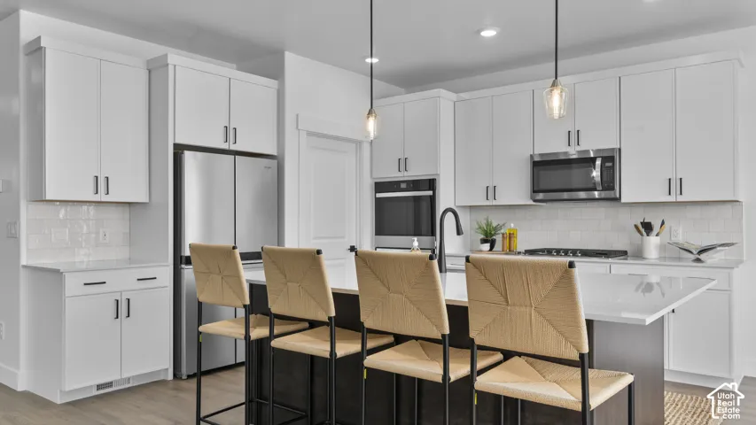 Contemporary kitchen featuring white cabinetry, stainless steel appliances, a center island with seating, and pendant lighting