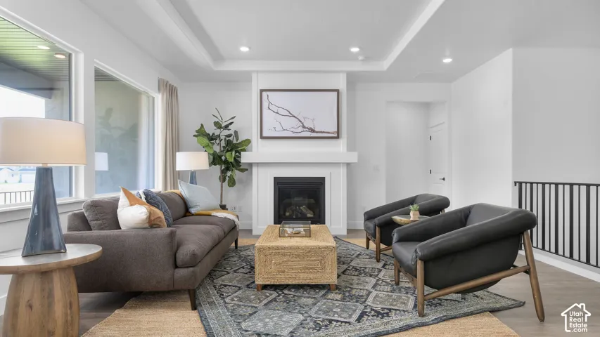 Living area featuring a fireplace with a mantel, tray ceiling, recessed lighting, and large windows