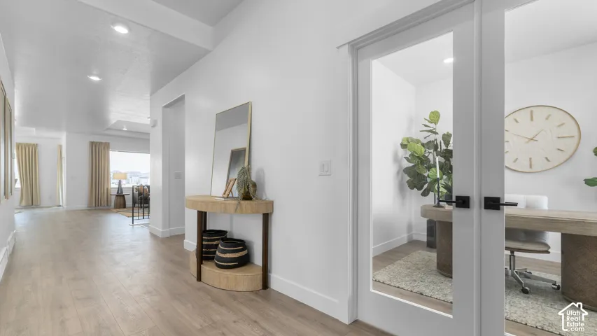 Light wood-finish flooring extending through the entry, white walls, recessed ceiling lighting, and a room with a frosted glass door