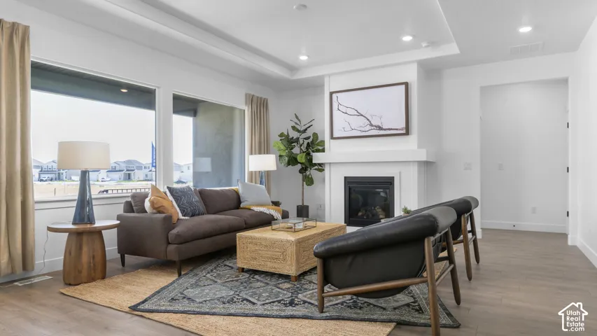 Recessed lighting, wood-finish flooring, large windows, tray ceiling, and a fireplace with a white mantel