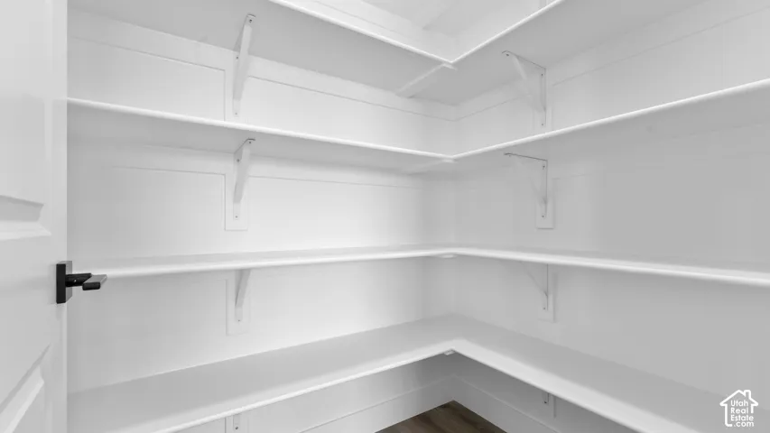 Walk-in pantry with ample white shelving, shiplap ceiling detail, and wood-finish flooring