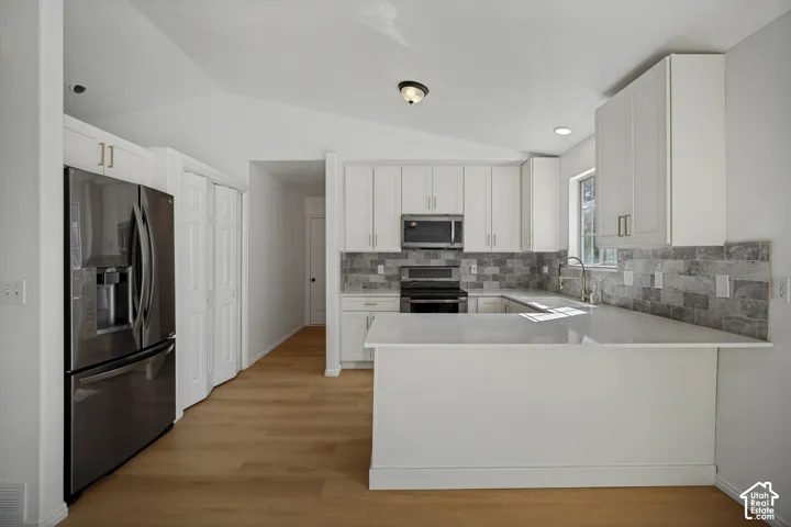 Kitchen featuring light wood-finish flooring, white cabinetry with gold-toned hardware, stainless steel appliances, a light-toned countertop, and a gray tile backsplash