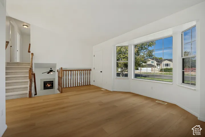Wood-finish flooring, bay window, carpeted staircase with wood railing, recessed fireplace, and ceiling fan