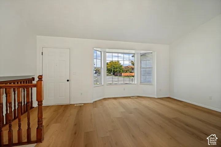 Wood-finish flooring throughout, white painted walls, and a bay window with street scenery