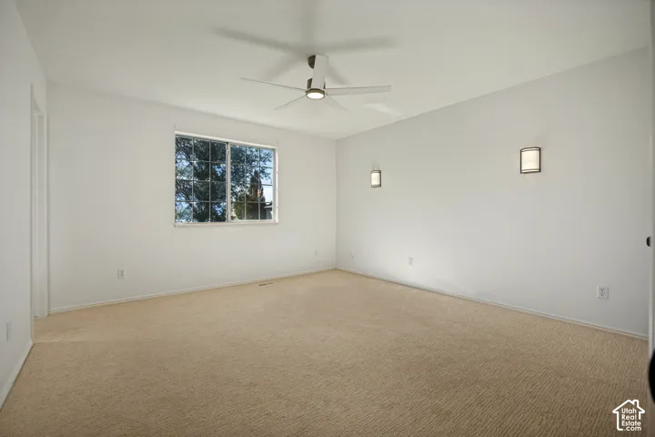 White walls, carpet flooring, window with grid panes, ceiling fan, and two wall sconces
