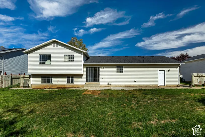 Expansive green lawn, light-colored siding, dark shingle roof, sliding glass patio door, and a white exterior door