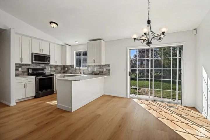 Kitchen featuring white cabinetry, gray tile backsplash, stainless steel appliances, wood-finish flooring, and a sliding glass door