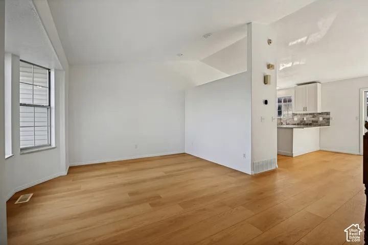 Wood-finish flooring throughout, bay window with louvered blinds, vaulted ceiling, white cabinetry with hardware, and tile backsplash