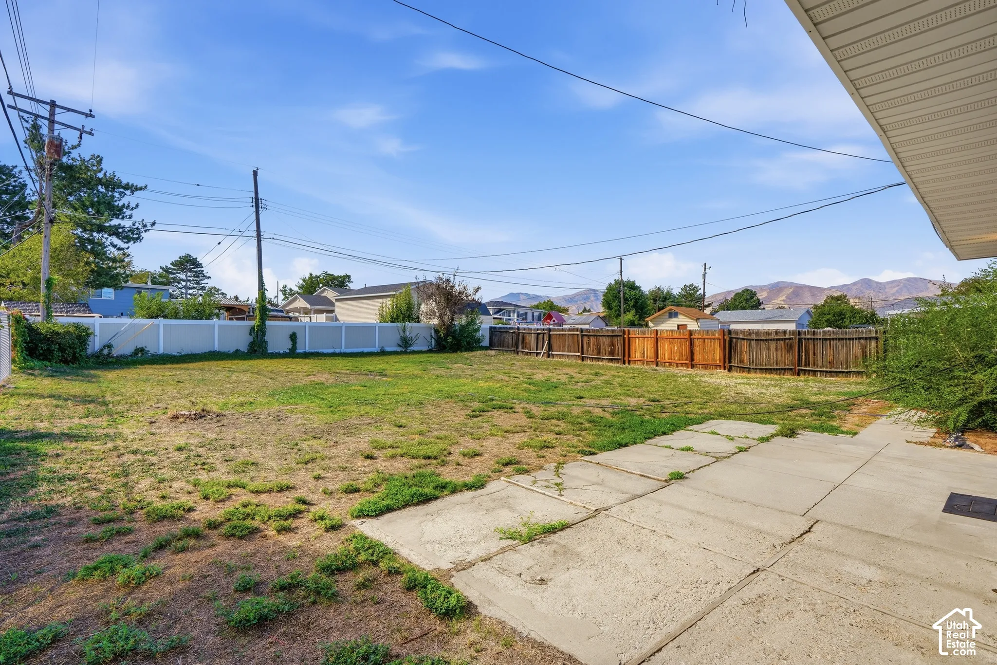 Expansive backyard with a concrete patio, wood fencing, and a white vinyl fence