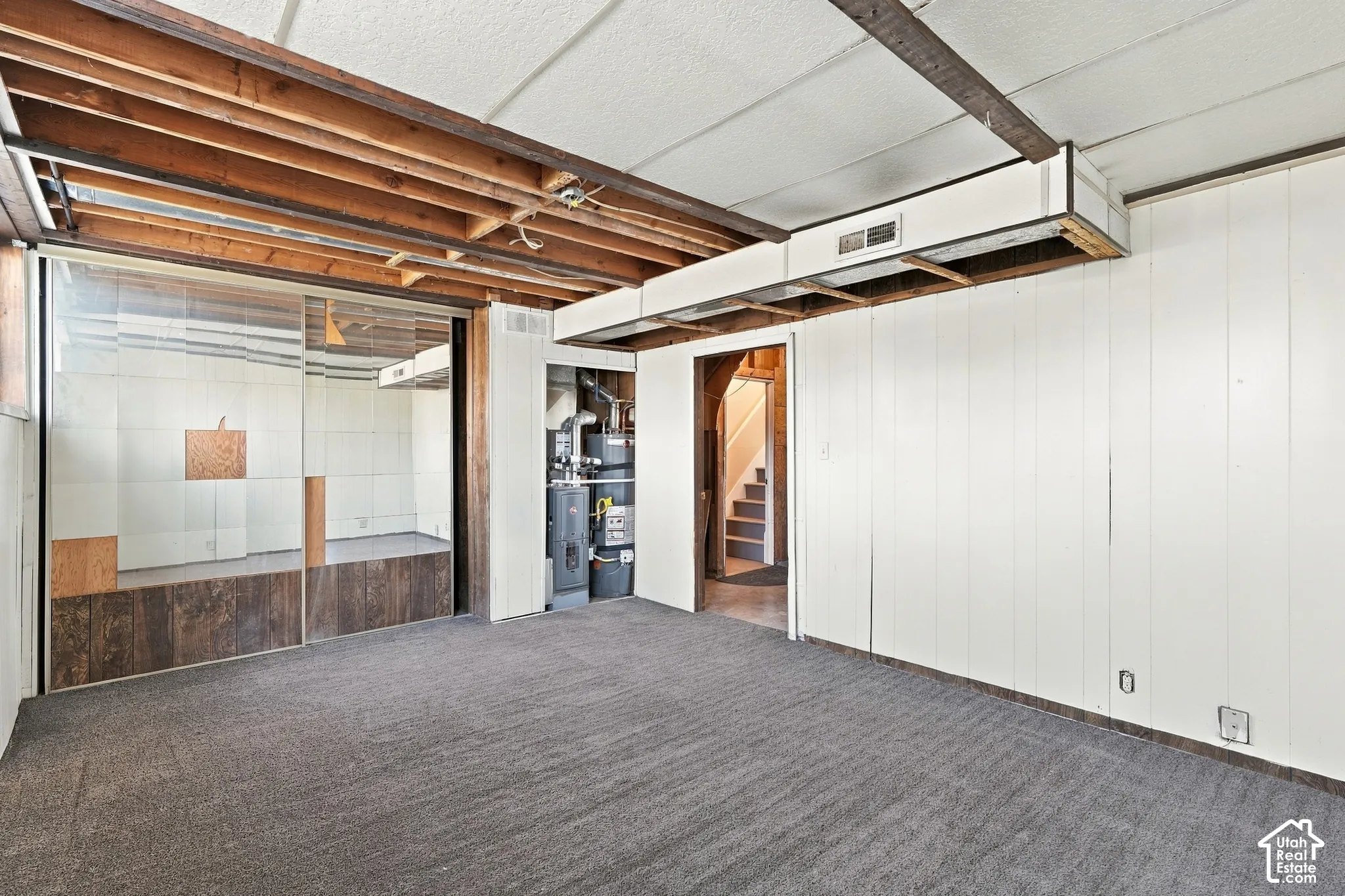 Carpeted flooring with exposed ceiling joists, white paneled walls, and a glass-enclosed space