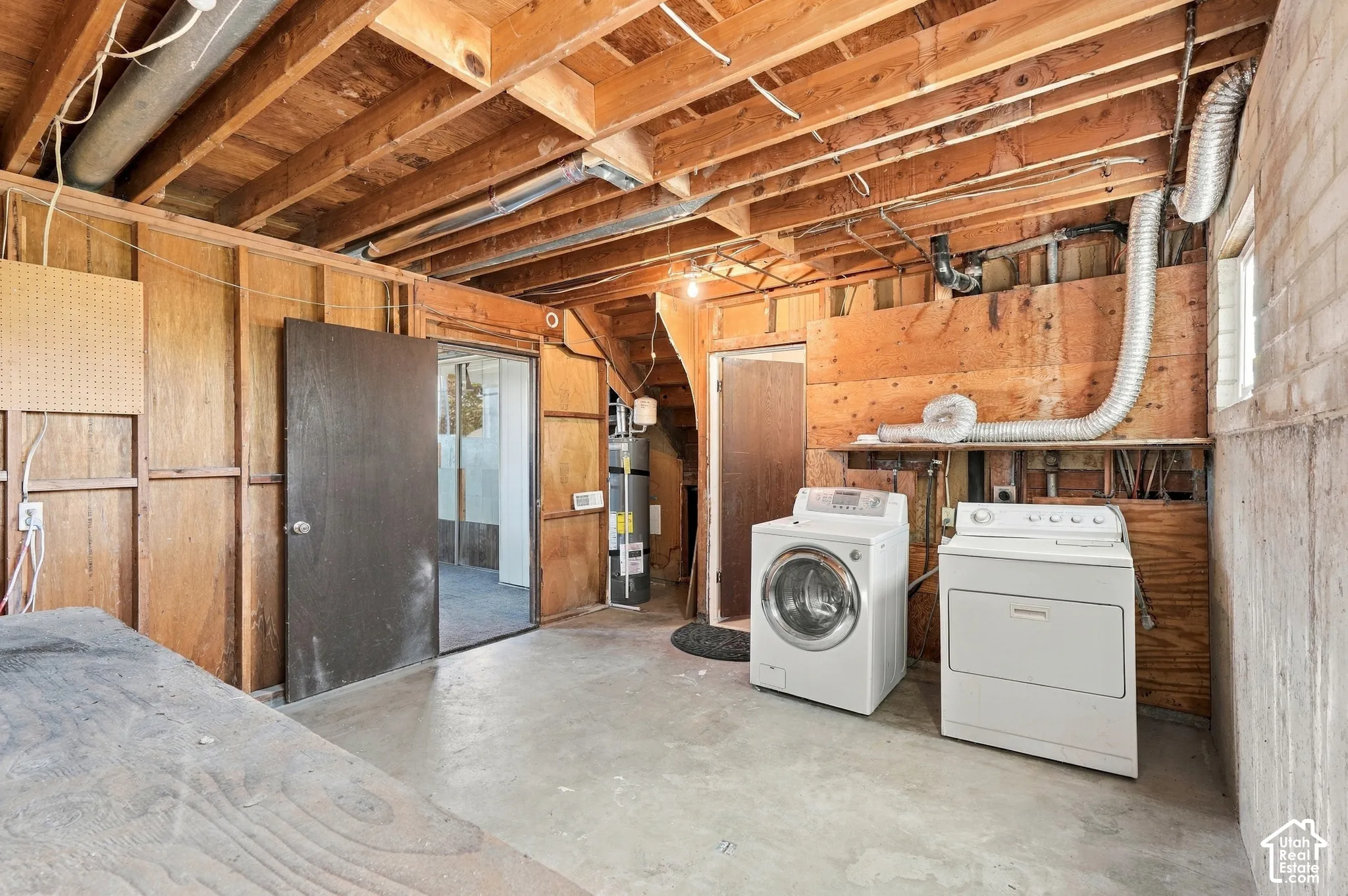 Unfinished basement with exposed ceiling joists, concrete flooring, and a dedicated laundry area