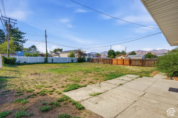 Expansive backyard with a concrete patio, wood fencing, and a white vinyl fence