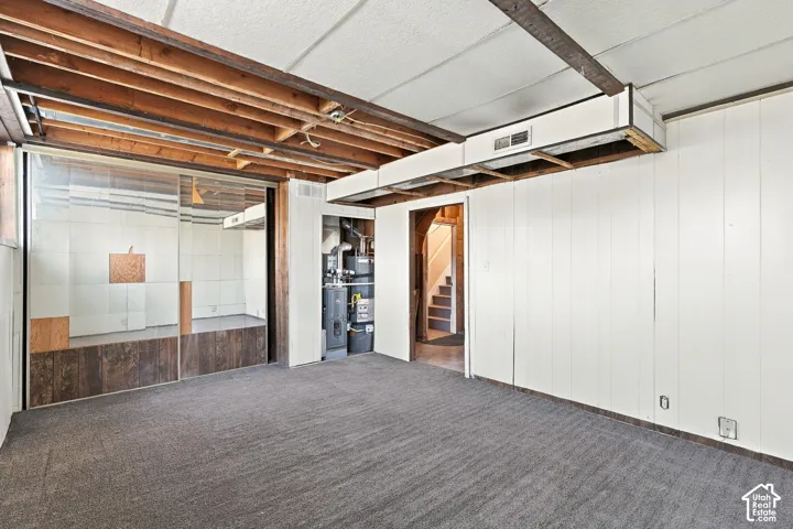 Carpeted flooring with exposed ceiling joists, white paneled walls, and a glass-enclosed space