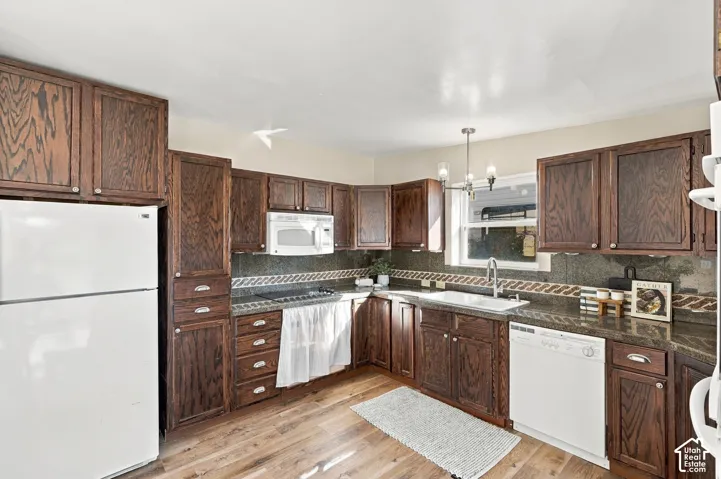 Wood-finish flooring, dark wood cabinetry, a white basin sink, and a multi-tone tile backsplash