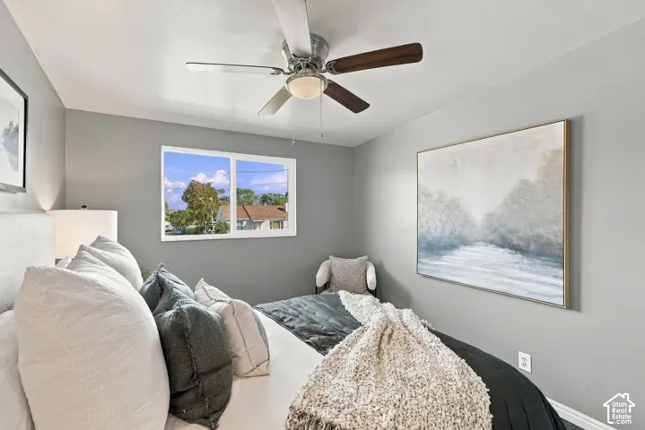 Window with white framing, ceiling fan with wood-finish blades and integrated lighting, gray wall paint, and white trim