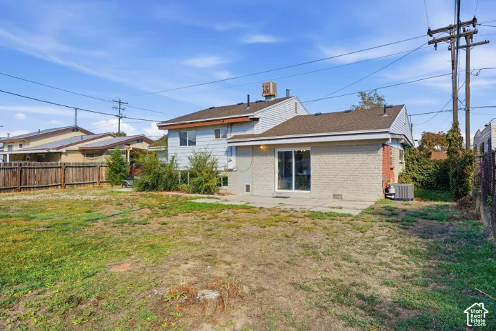 Rear exterior featuring a sliding glass door, patio, light-colored brick exterior, and partial wood fencing