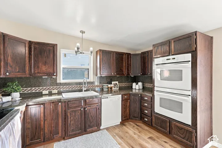 Wood-finish flooring, dark wood cabinetry, white double wall oven, and a white integrated sink