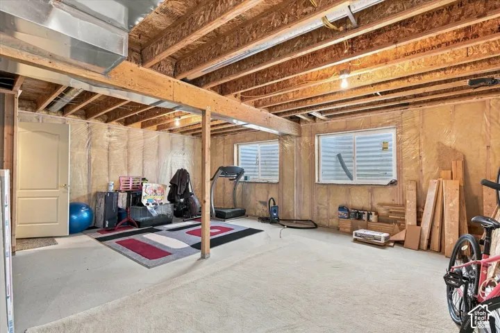 Unfinished basement with exposed ceiling joists and support beams, featuring two windows and a white paneled door
