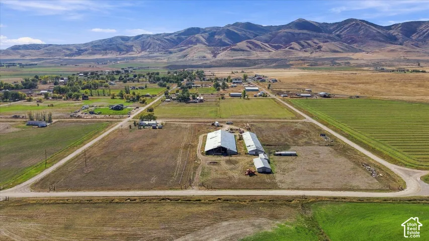 Expansive agricultural property featuring multiple outbuildings, cultivated fields, and a mountainous backdrop