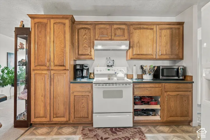 Wood-finish cabinetry with crown molding, integrated pantry storage, dark countertops, a white range, and patterned flooring