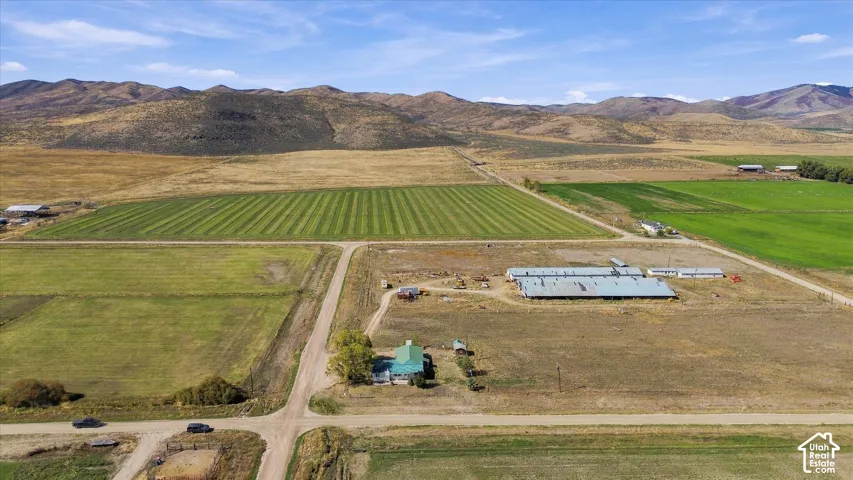 Expansive property featuring cultivated fields, a residential structure with a green roof, multiple outbuildings, and a mountainous backdrop