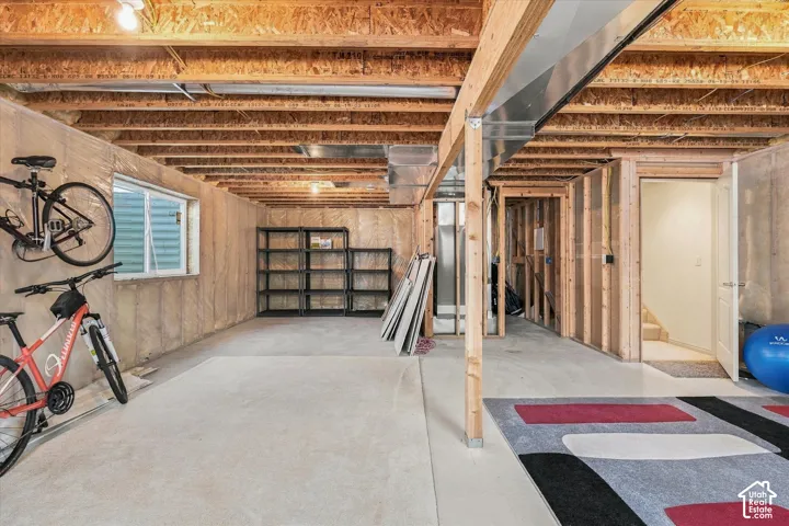 Unfinished basement featuring exposed wood joists and structural beams, a dedicated egress window, and framed interior walls, offering potential for future customization
