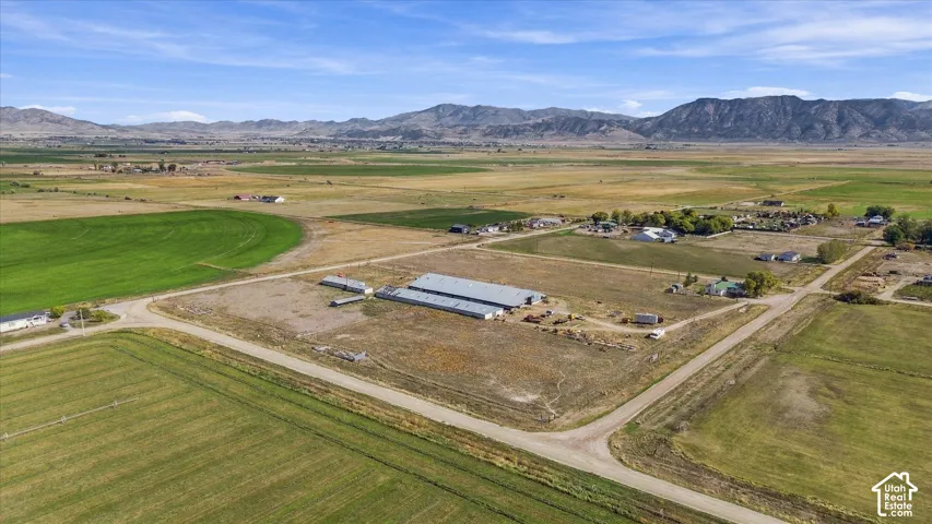 Expansive open land featuring agricultural fields, multiple buildings, and mountain scenery