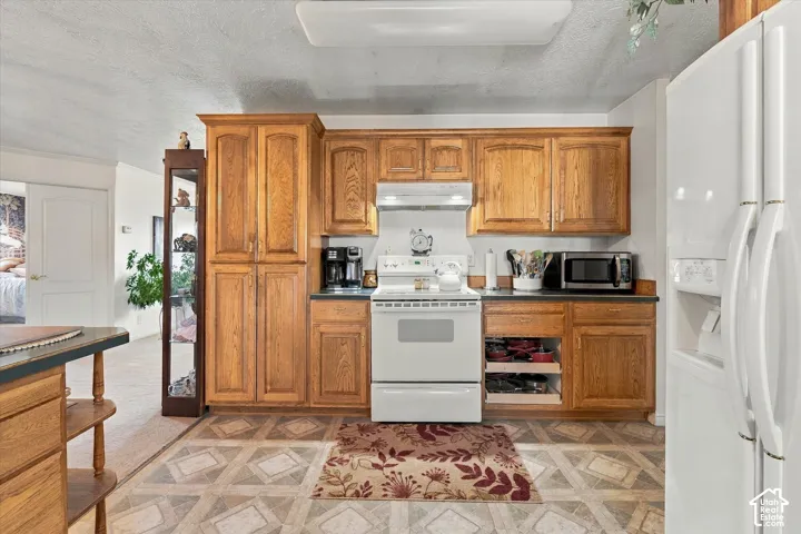 Kitchen featuring wood cabinetry, white electric range, white side-by-side refrigerator, and patterned vinyl flooring