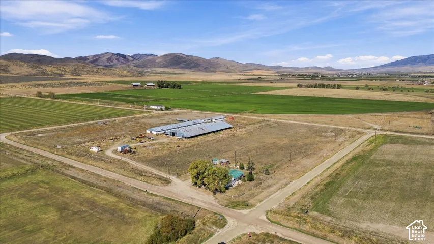 Expansive rural property featuring multiple agricultural structures, cultivated fields, and surrounding mountain ranges