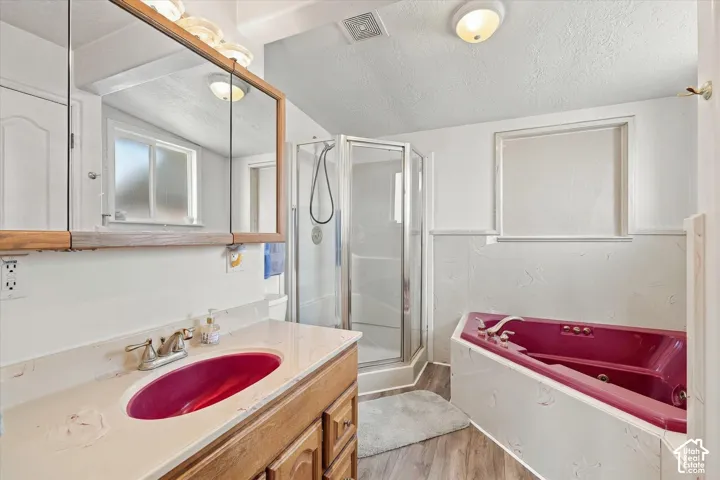 Corner shower with glass enclosure, single vanity with countertop, wood-finish flooring, and built-in tub