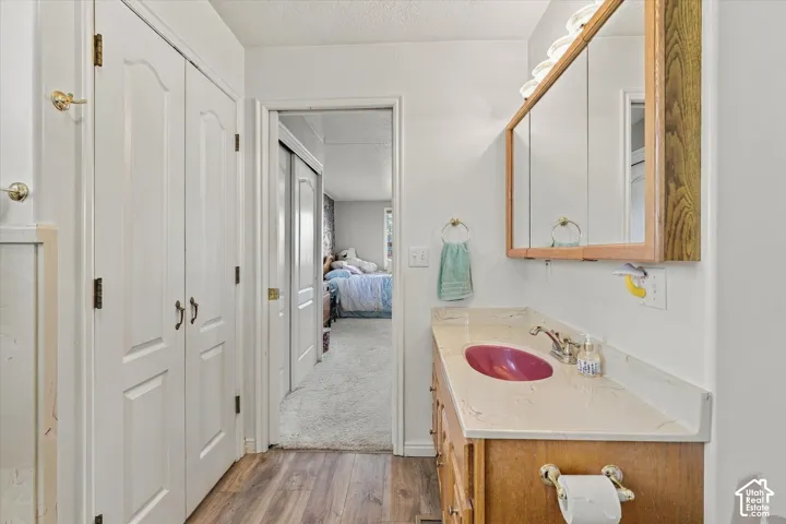 Wood-finish flooring, white paneled bifold doors, wood vanity with light-toned countertop, and medicine cabinet with integrated lighting