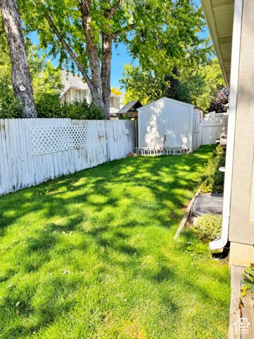 Fenced yard with a storage shed, established trees, and green lawn