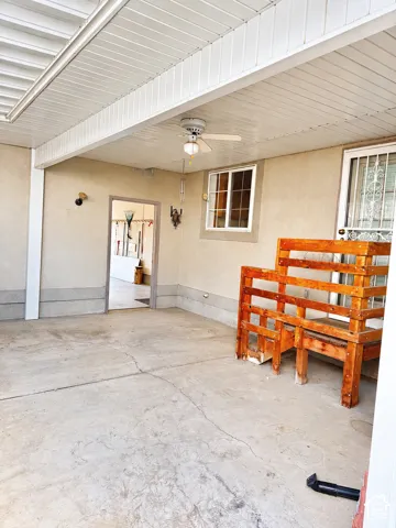 Covered patio area with a ceiling fan, concrete flooring, and an exterior door