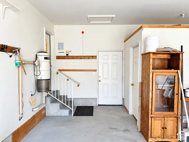 Concrete floor, integrated central vacuum system, interior staircase with white railing, paneled interior door, and wooden trim accents