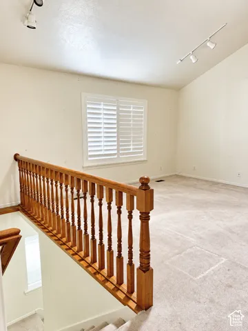 Hardwood staircase railing with turned spindles, white plantation shutters, vaulted ceiling, and track lighting