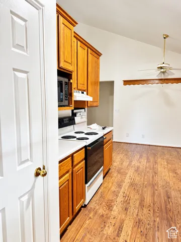 Kitchen featuring wood-finish flooring, wood cabinetry, white countertops, built-in microwave, and electric range